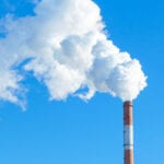 Time to put the foot down? Pipe with white smoke against the background of blue sky and copy space. emission of steam and smoke into the atmosphere