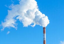 Time to put the foot down? Pipe with white smoke against the background of blue sky and copy space. emission of steam and smoke into the atmosphere