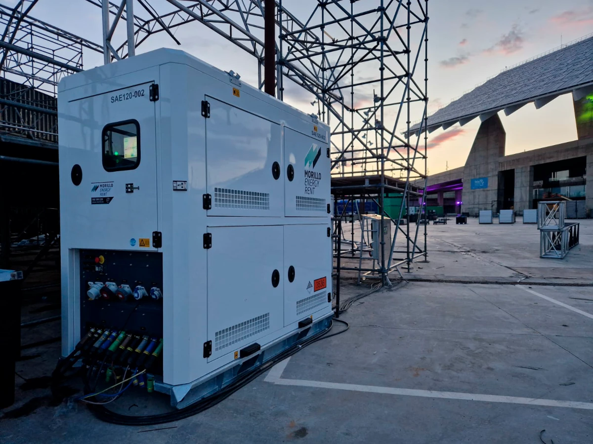 White cuboidal enclosure with wires trailing out, situated within a scene resembling backstage at an open air musical event