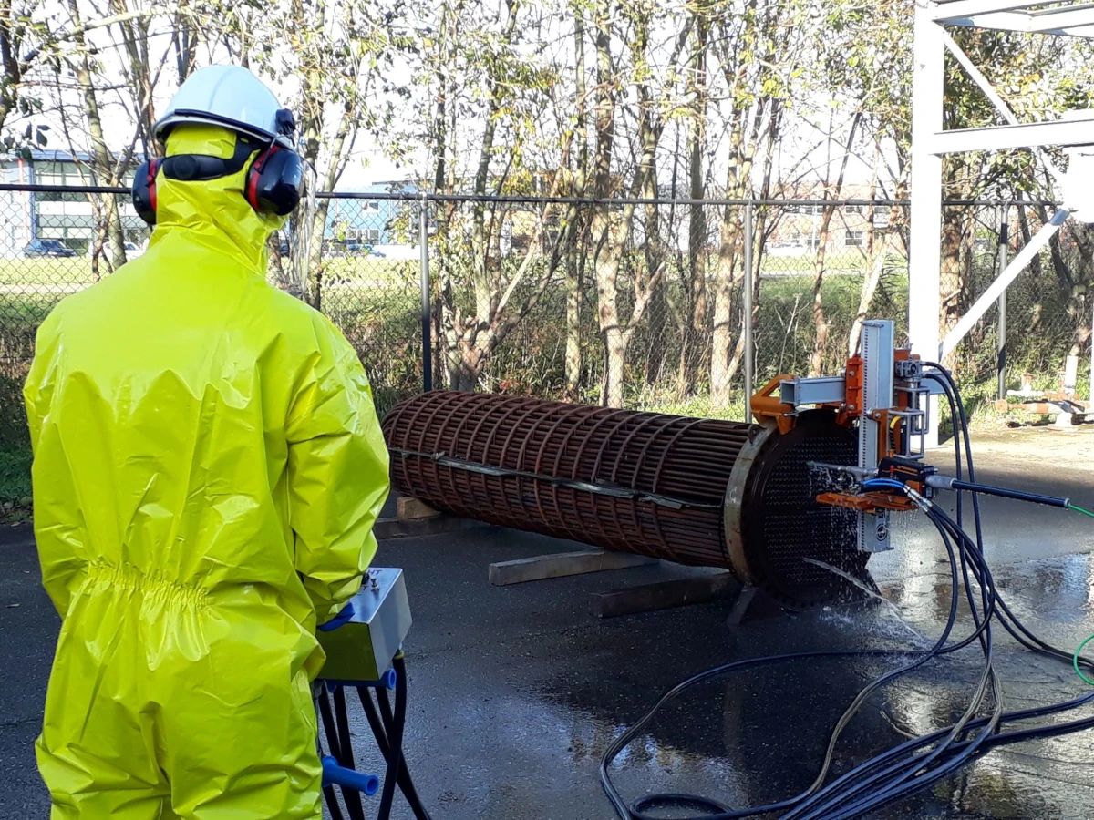 Jetting equipment operator in waterproof clothing, hard hat and ear protection, with cylindrical equipment in the background