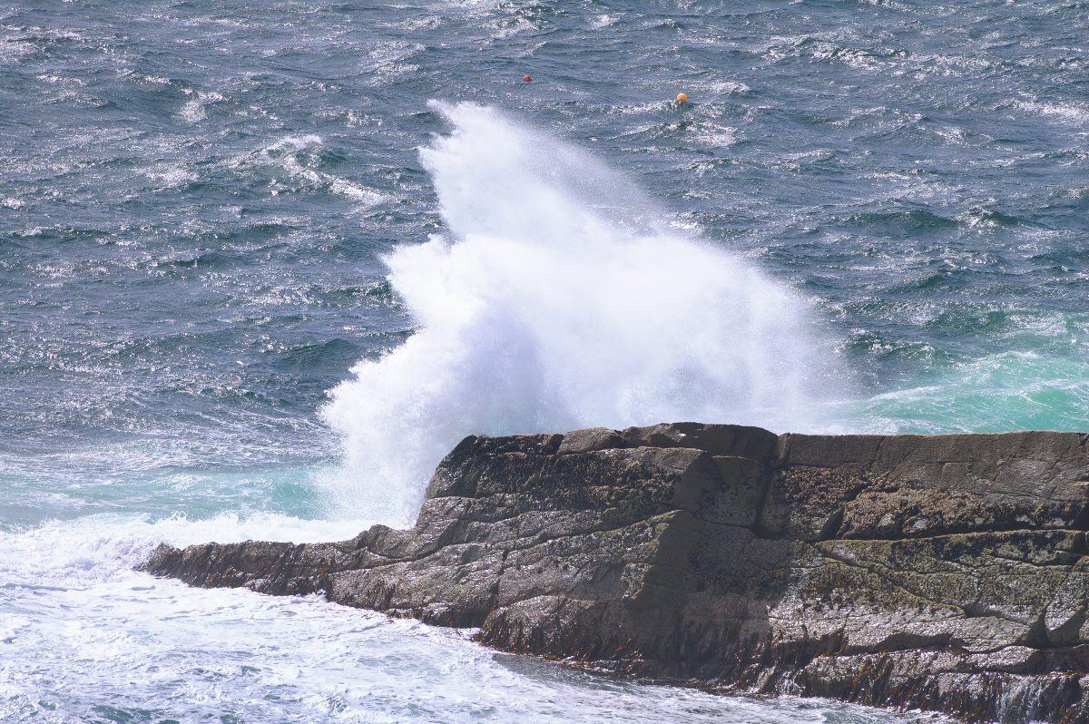 A wave crashing against a rocky promontory in a Scottish location