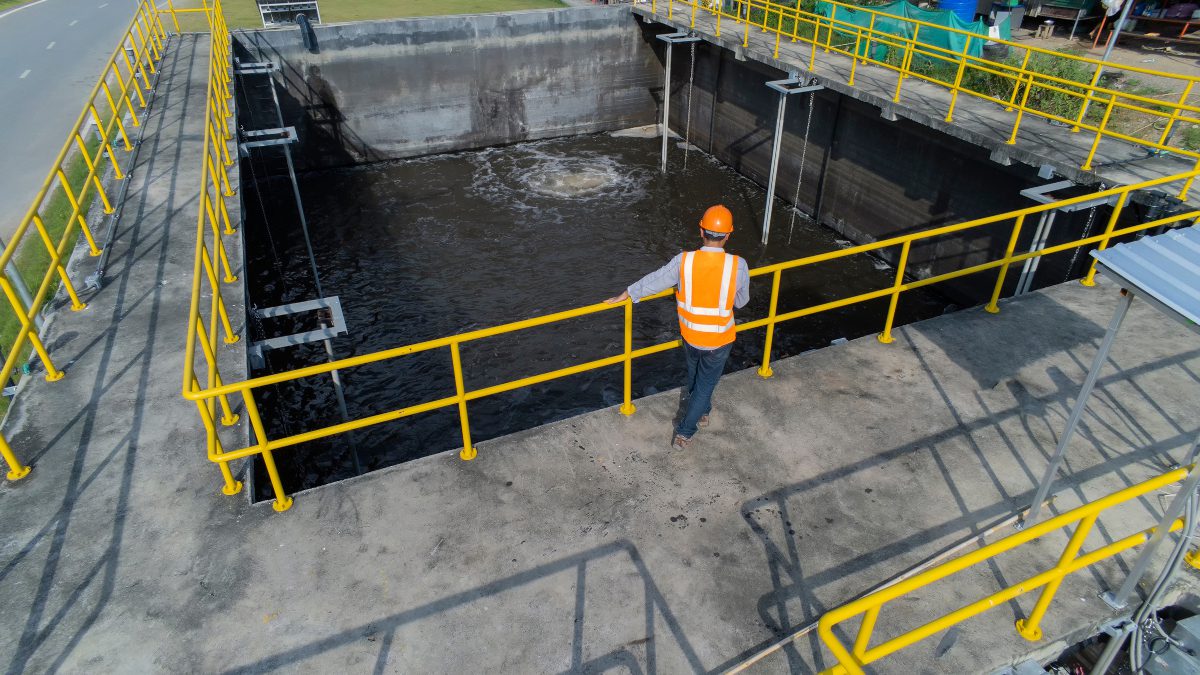 Technical worker standing at the edge of a wastewater treatment pond, looking down into it