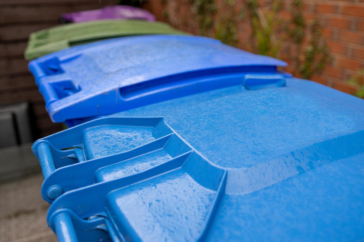 UK wheelie bins for recycling, with light blue, dark blue, green and pink lids visible