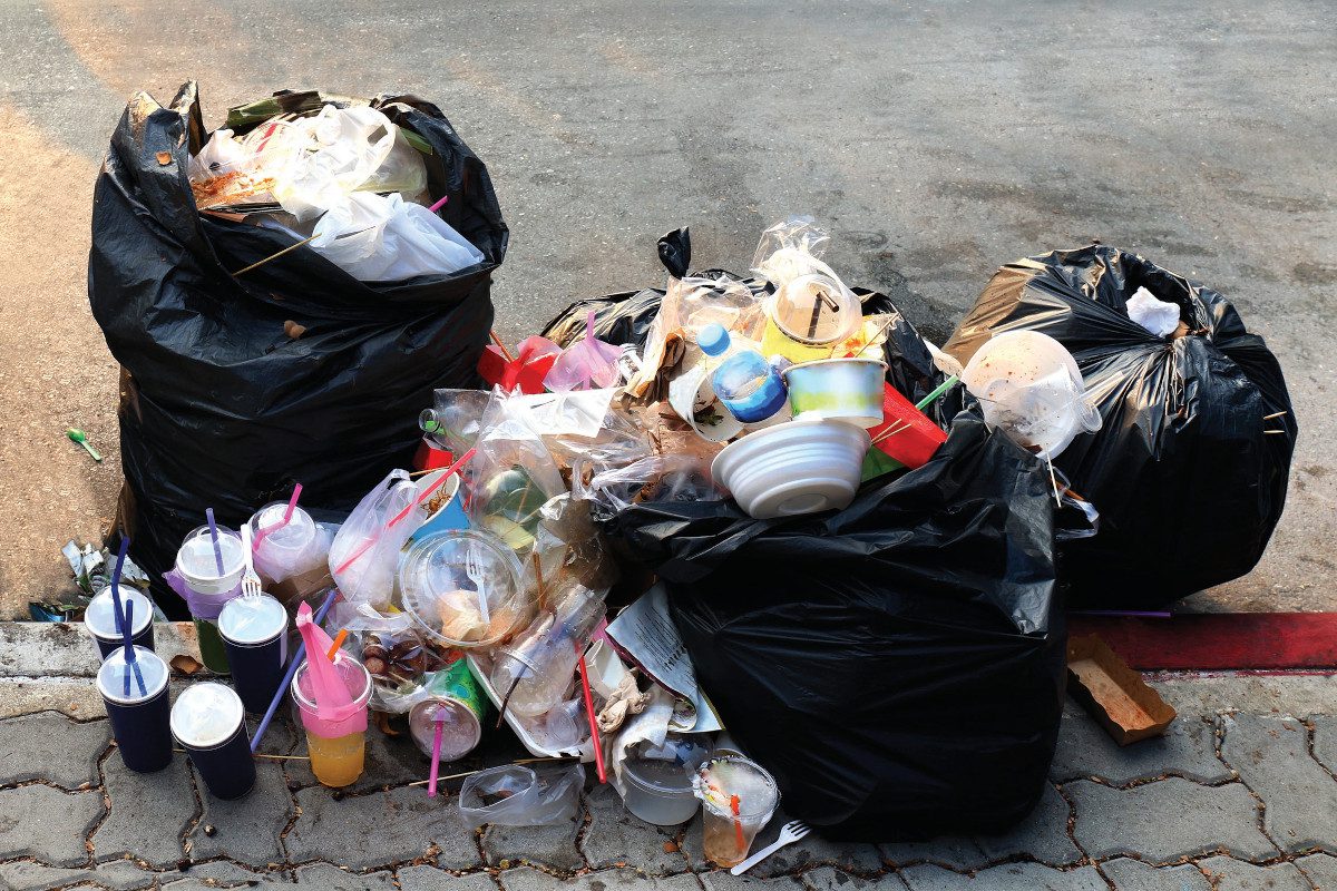 Black household waste bags overflowing with waste such as plastic cups and tubs