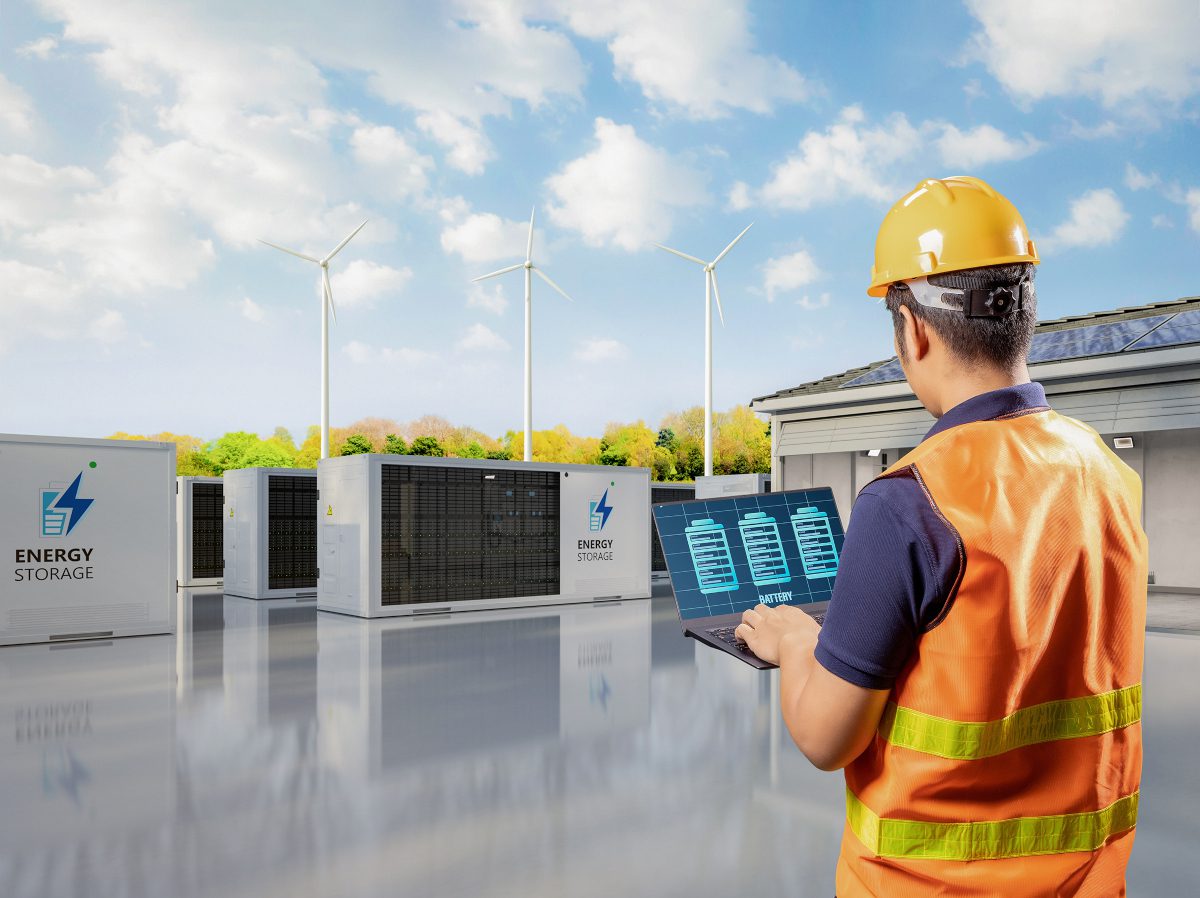 Energy storage site with cuboidal enclosures and technician in hard hat and luminous vest in the foreground