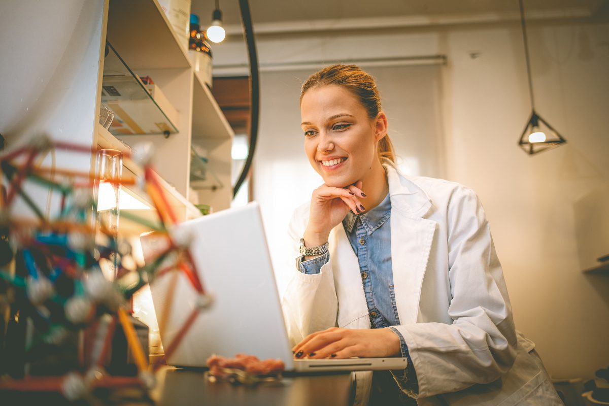 Female scientist in white coat sitting at a computer with plastic models of sitting in the foreground 