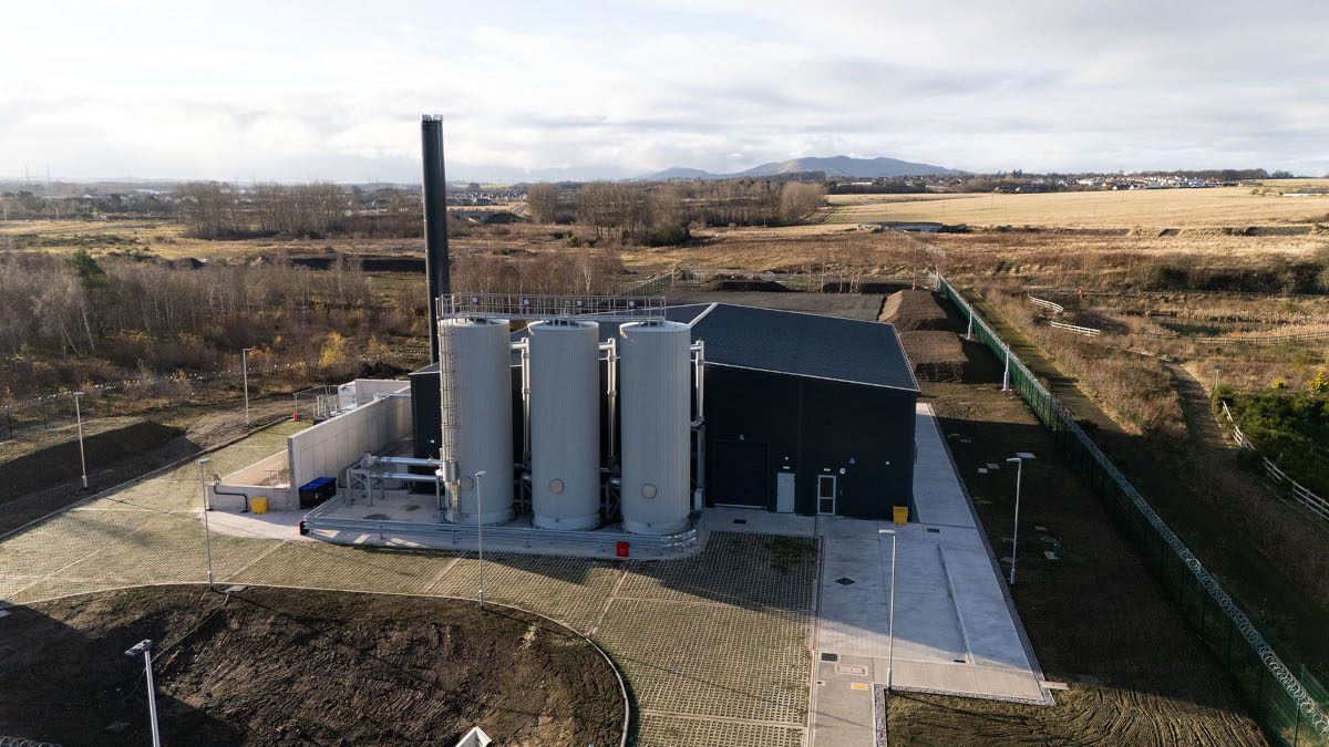 Industrial building complex situated within rural landscape of ochre, dirt-coloured ground and grey sky