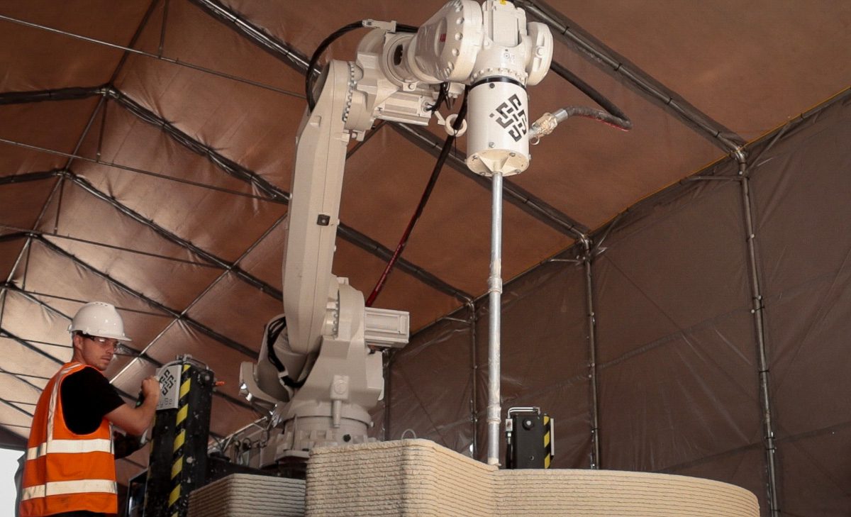 Technician in hard hat operating a large industrial assembly with a drill attachment that seems to be bearing down on a piece of material