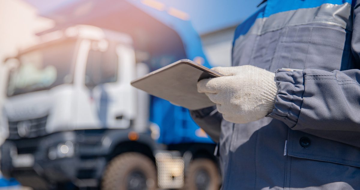 Close up of uniformed hand and arms using PDA with lorry in the background