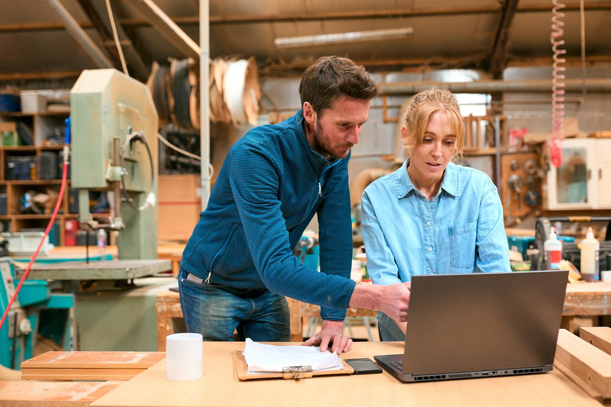 Man and young woman looking at laptop, wearing casual clothes, in workshop-like space