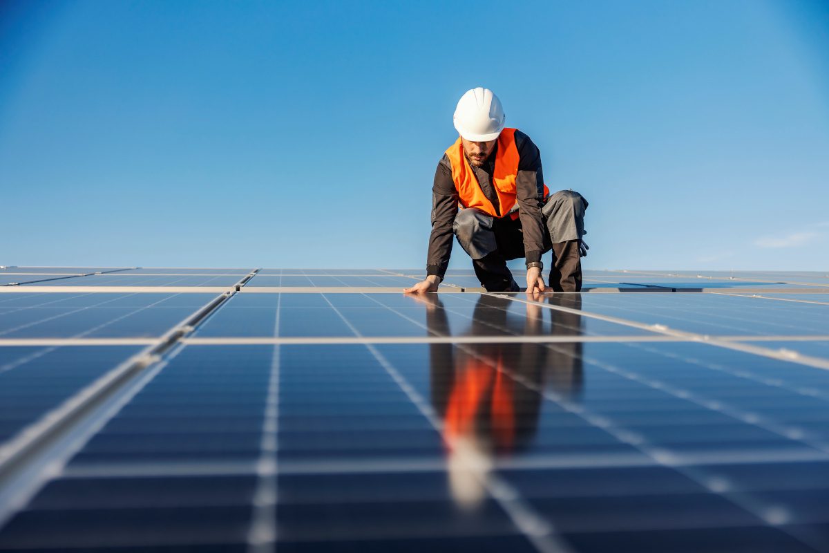 Workman crouched atop a solar panel laid flat