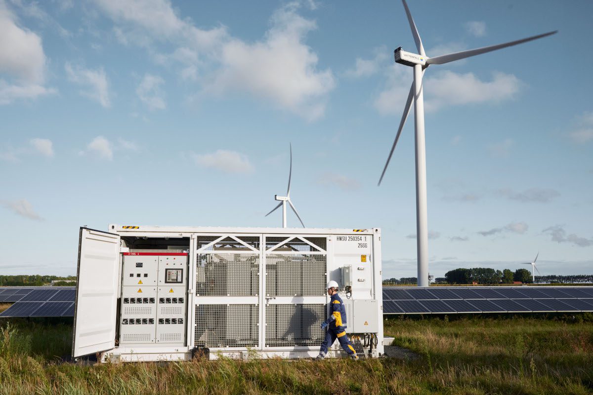 wind and solar energy in outdoor location, with electrical systems enclosure in foreground and a uniformed worker in hard hat