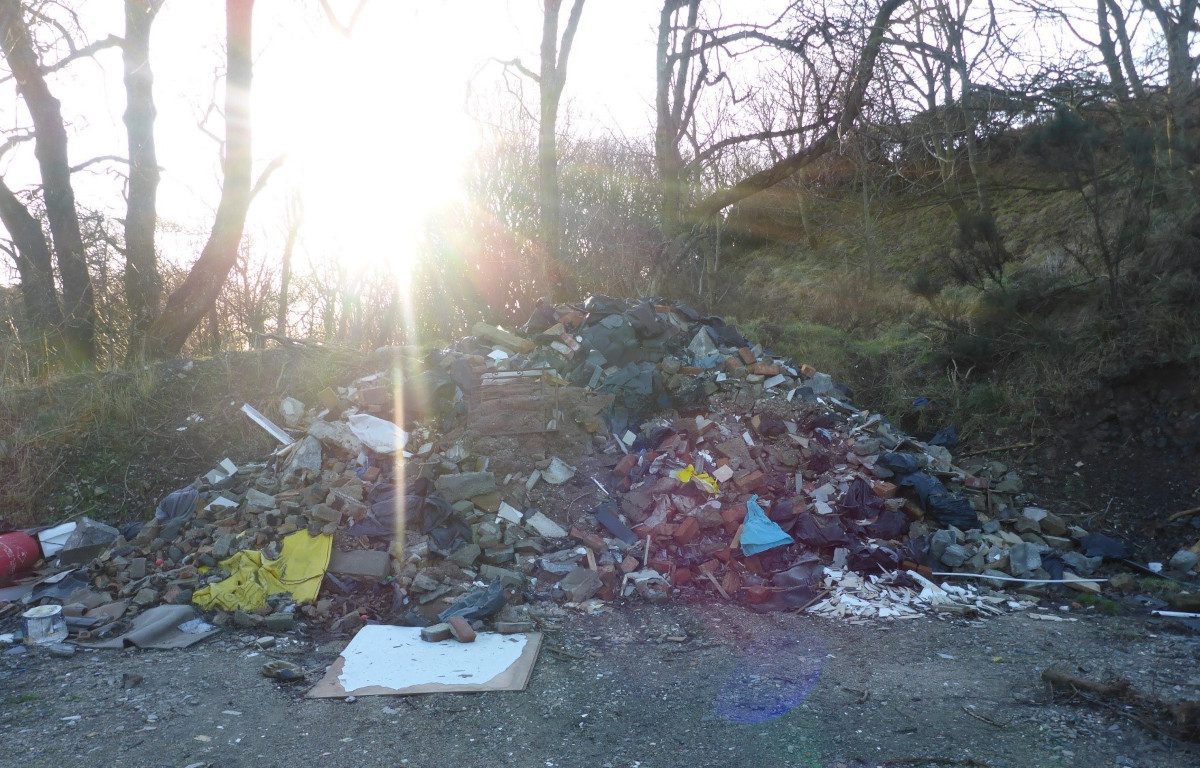 An outdoor site in a rural location with matrresses and other waste lying around