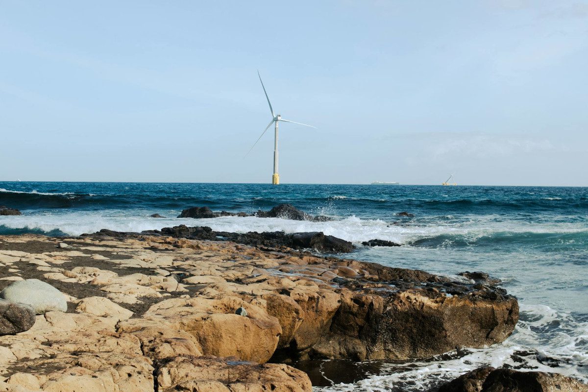 Rocky shoreline with wind turbine in view in the distance out to sea