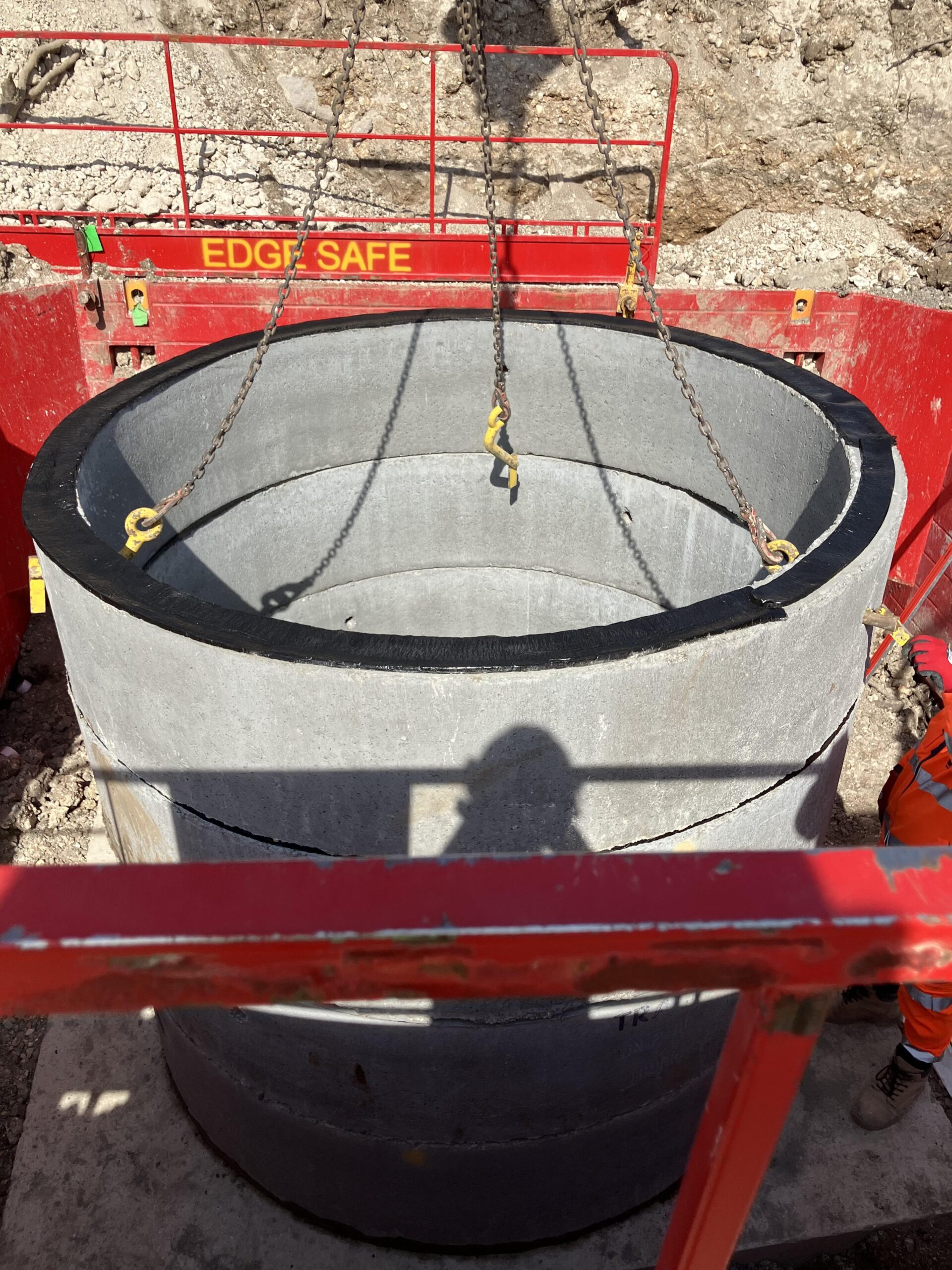 Cylindrical structure, possibly made of concrete to which are attached chains, as if it is being lowered into position by equipment