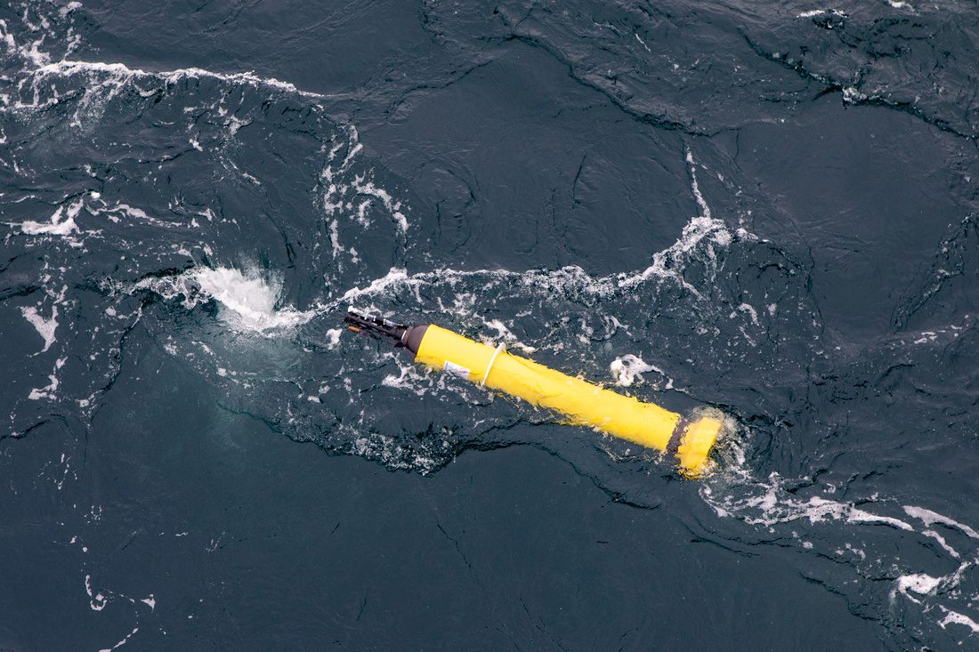 Yellow, cylindrical device - with torpedo-like shape - floats at the surface of the ocean, as seen from slightly above and to one side