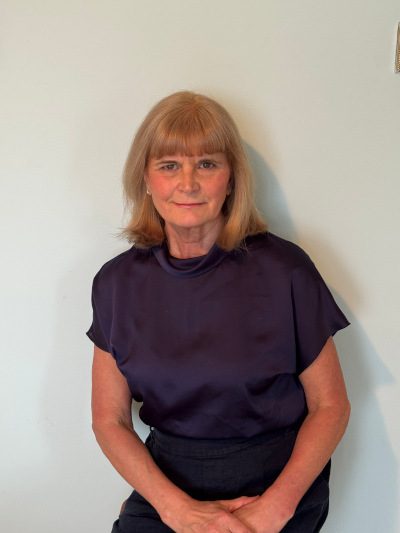A woman with reddish hair and black blouse smiles at the camera