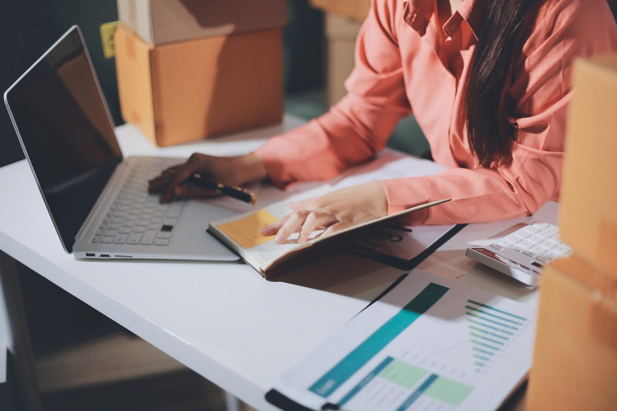 Torso, arms and desk of office worker working with documents and a laptop computer, possibly a business owner or accountant