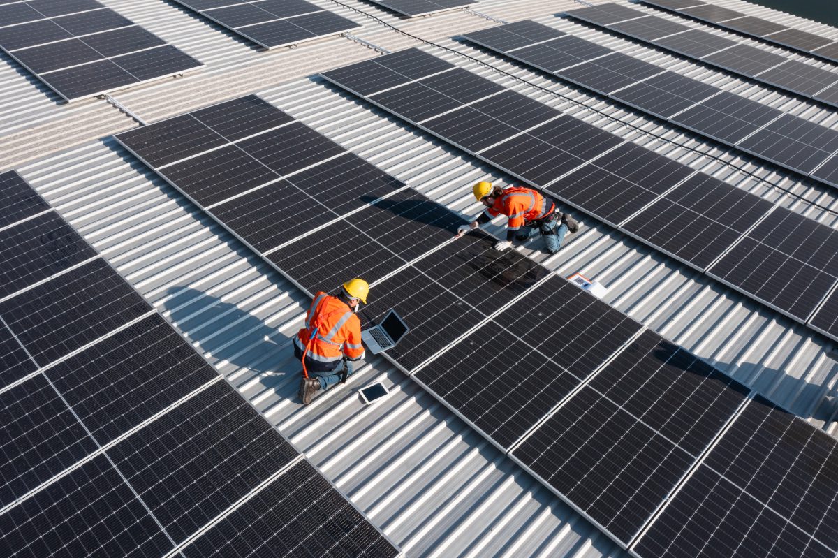 Technicians laying-out rooftop solar panels on a large, flat roof space