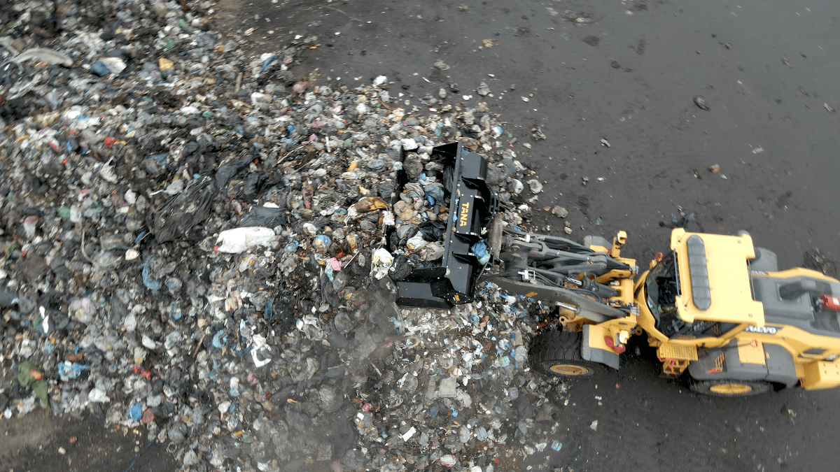 Aerial view of wheel loader with waste shredding attachment, working on waste at a rubbish tip