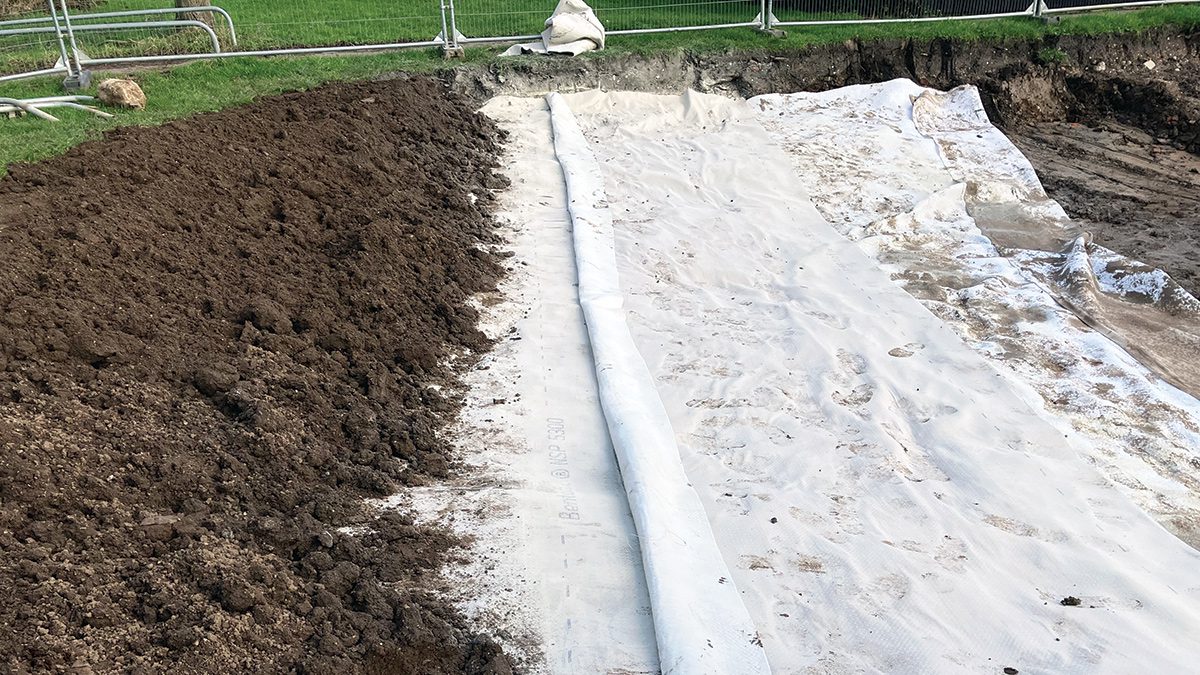 A geocomposite waterproof liner being installed in a large excavated sustainable drainage (SuDS) basin, with earth backfill alongside, as part of the Derringham Aqua Greens flood resilience project in Hull