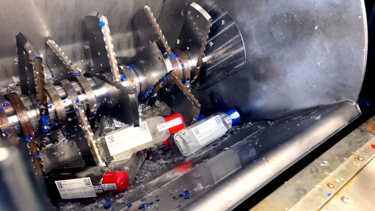 Plastic laboratory sample bottles being processed inside an industrial shredding machine.