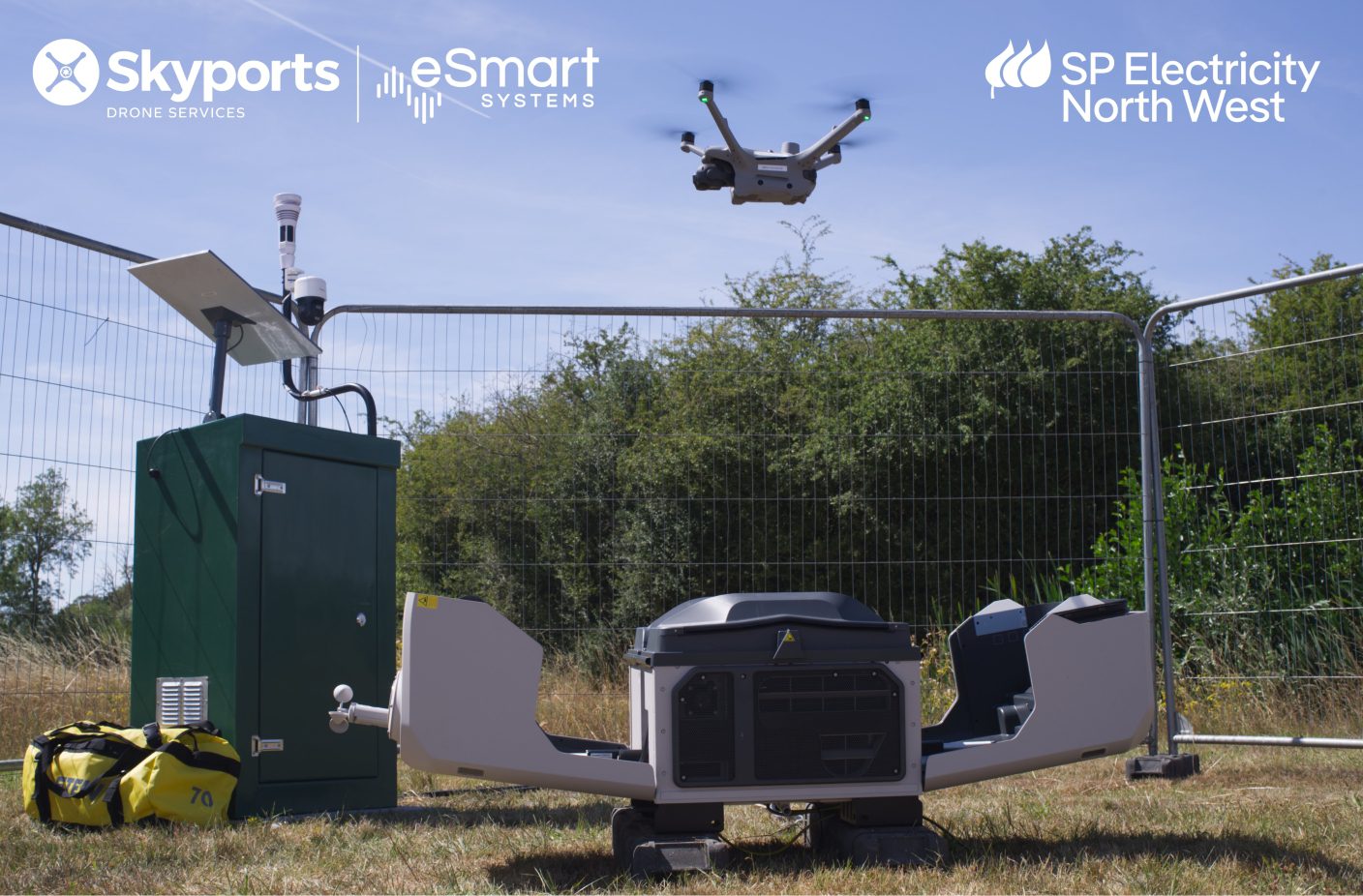 Drone flying above an automated docking station and monitoring equipment at a fenced outdoor site